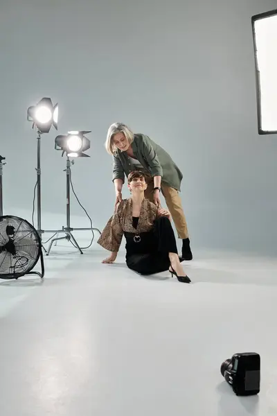 Middle-aged woman photographs her partner in a photo studio while kneeling down beside her. — Stock Photo