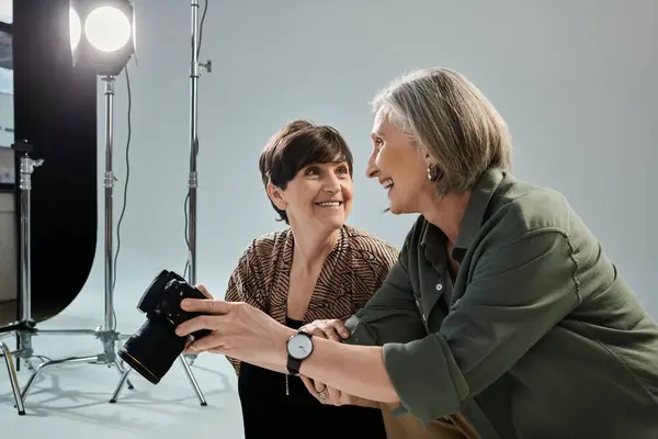 Ein lesbisches Paar mittleren Alters in einem Fotostudio; eine Frau benutzt eine Kamera, und andere lächeln — Stockfoto