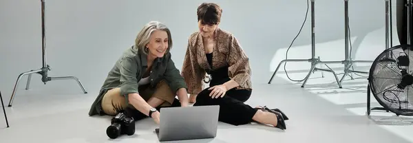 Pareja lesbiana de mediana edad trabajando juntos en el portátil, un fotógrafo y el otro un modelo. - foto de stock