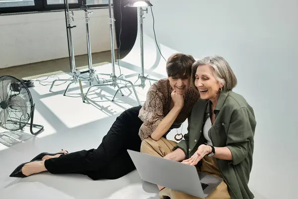 Couple lesbien d'âge moyen assis paisiblement sur un sol blanc dans un studio de photo — Photo de stock
