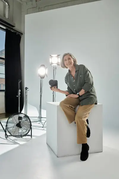 Fotógrafo de meia-idade com câmera sentada em estúdio. — Stock Photo