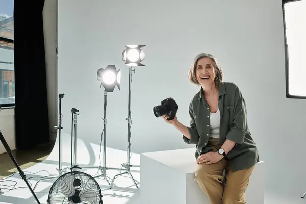 Fotógrafo de meia-idade alegre com câmera sentada em estúdio. — Fotografia de Stock