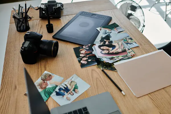 Mesa de madera con portátil y fotos, mostrando el trabajo y la creatividad en un estudio moderno. - foto de stock