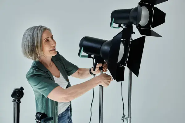 Mujer de mediana edad sostiene una luz mientras establece un trípode en un estudio fotográfico profesional - foto de stock