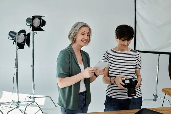 Una mujer de mediana edad sostiene una cámara delante de su pareja en un moderno estudio de fotografía profesional. - foto de stock