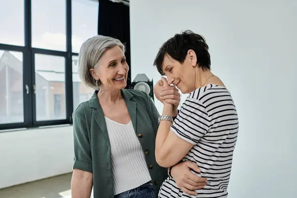 Two women, middle-aged, stand by a window, sharing a candid moment of companionship and collaboration in a modern studio. — Stock Photo