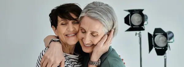 Middle-aged lesbian couple hugging each other warmly in a modern photo studio setting. — Stock Photo