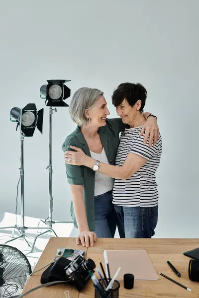 Two middle-aged women hug in front of a camera in a modern photo studio. — Stock Photo
