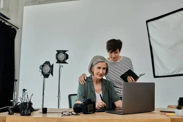 Couple sit beside each other as they work on a laptop computer together in a professional photo studio. — Stock Photo