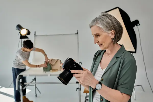 A middle-aged woman holds a camera in a modern photo studio setting. — Stock Photo