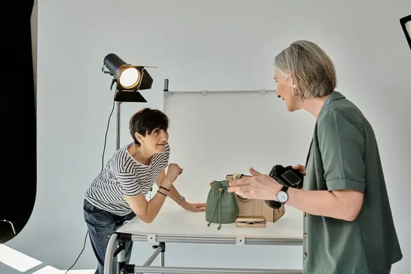 A middle aged women stand in a modern photo studio, smiling as they work together in front of a camera. — Stock Photo