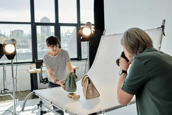 A middle-aged woman takes a picture of purses in a professional photo studio setting. — Stock Photo