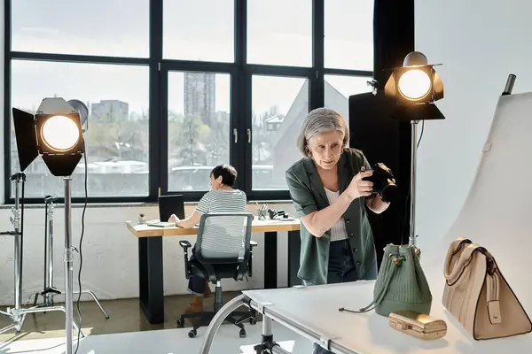Uma mulher de meia-idade tira uma foto de bolsas em uma configuração moderna estúdio de fotos. — Fotografia de Stock
