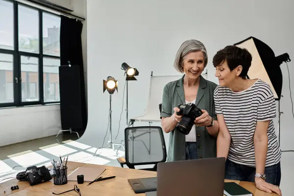 Middle-aged lesbian couple standing together, engrossed in work on a laptop in a professional modern photo studio. — Stock Photo
