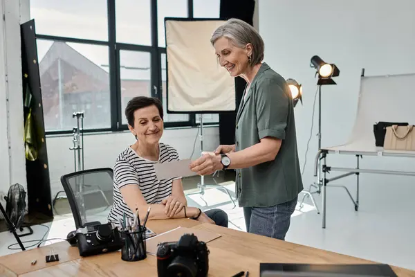 A middle-aged woman sits at a table in front of a camera o in a modern photo studio. — Stock Photo