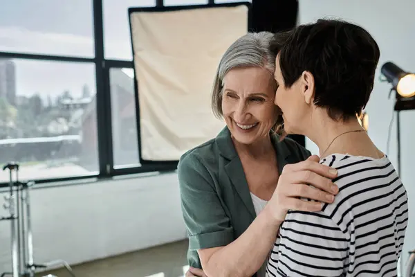 Middle-aged lesbian couple hugging warmly in a modern photo studio, fostering a sense of collaboration and unity. — Stock Photo