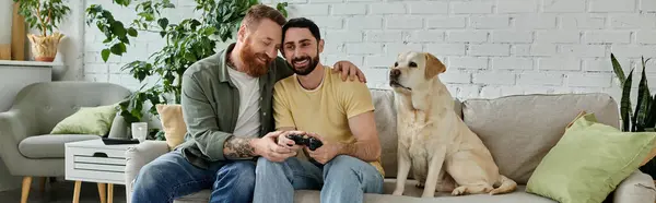 Бородата гомосексуальна пара захопилася відеоіграми з їхнім вірним лабрадором на дивані. — стокове фото