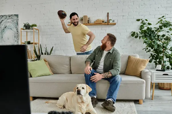 Um homem com barba senta-se em um sofá com um Labrador, ambos absorvidos em uma partida de esportes na TV. — Fotografia de Stock