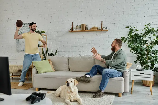 Barbudo hombre y perro ver los deportes en el sofá en acogedora sala de estar. - foto de stock