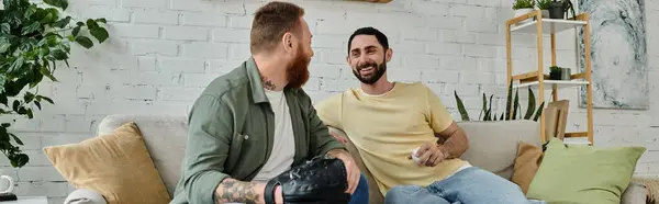 A couple of bearded men relax on top of a couch while watching a sport match