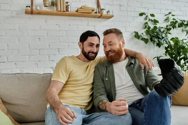 Um par de homens barbudos relaxar juntos em um sofá, assistindo a um jogo de esportes em sua sala de estar. — Fotografia de Stock