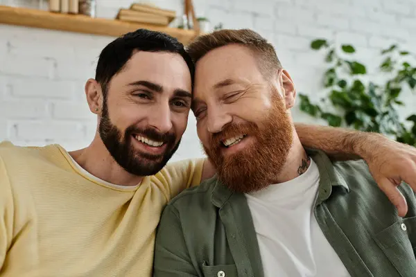 Dois homens, ambos com barba, relaxam em um sofá e abraçam em casa — Fotografia de Stock