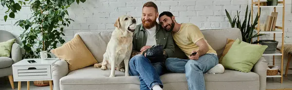 Dois homens com barbas sentados em um sofá, desfrutando de tempo de qualidade com seu Labrador, assistindo a um jogo de esportes na TV. — Fotografia de Stock