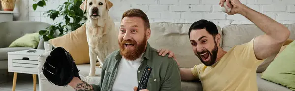Two bearded men and their Labrador dog sit atop a couch, engrossed in watching a sports match on TV in their living room. — Stock Photo