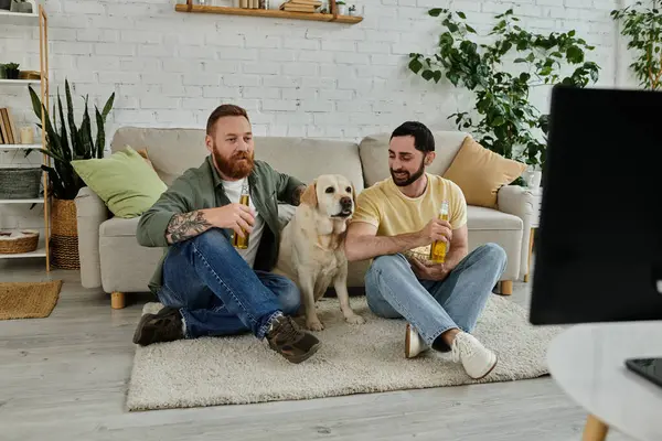 Two men with a dog watching sports on a couch in a cozy living room together. — Stock Photo