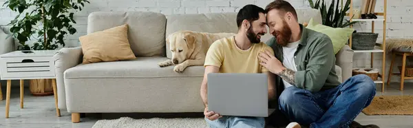 Dos hombres con barba se sientan encima de un sofá trabajando a distancia, acompañados por un perro labrador en una acogedora sala de estar. — Stock Photo