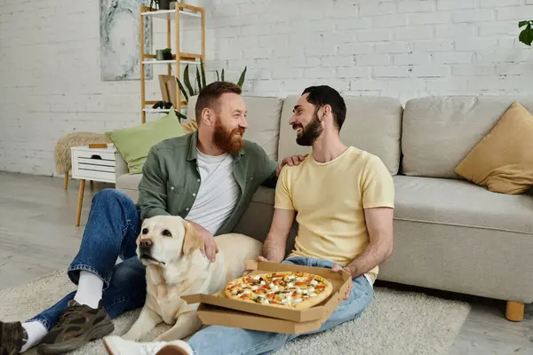 Двоє бородатих чоловіків сидять на підлозі, ділячись піцою з лабрадорським собакою в затишній обстановці у вітальні. — стокове фото