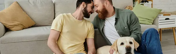 Zwei Männer, ein bärtiges schwules Paar, sitzen auf einer Couch neben einem freundlichen Labrador-Hund in gemütlicher Wohnzimmeratmosphäre.. — Stockfoto