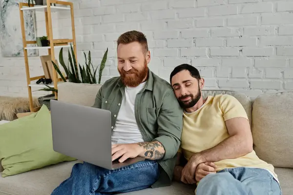Two men with beards sitting on a couch in a living room, focused on a laptop screen in front of them. — Stock Photo