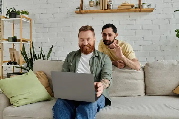 Bärtiges homosexuelles Paar in Laptop-Inhalt versunken, während es auf der Couch in einem gemütlichen Wohnzimmer sitzt. — Stockfoto
