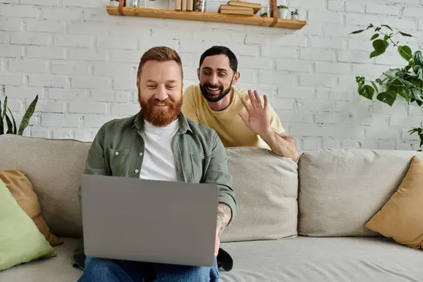 Два чоловіки, один бородатий, сидять на дивані, зосереджені на екрані ноутбука в затишній обстановці вітальні. — стокове фото