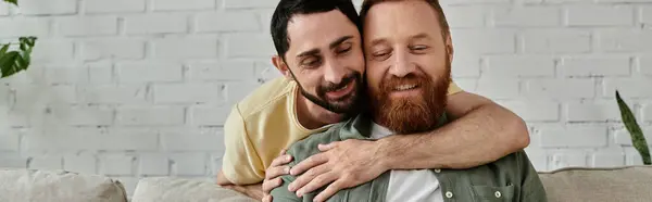 Due uomini barbuti che si abbracciano affettuosamente su un accogliente divano nel loro soggiorno. — Foto stock