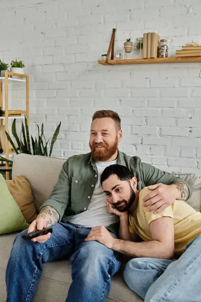 A couple of bearded men sit comfortably on a couch in their living room, enjoying quality time together. — Stock Photo