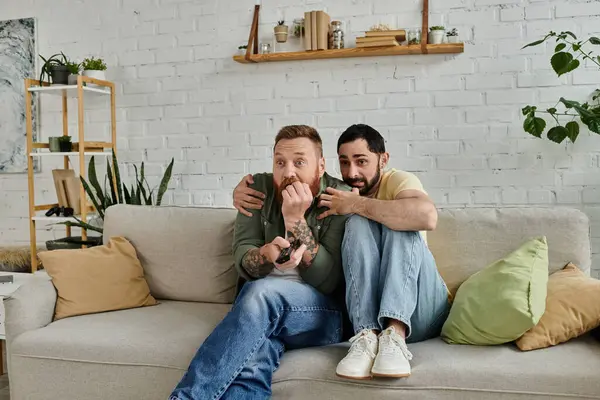 Two bearded men sitting on a couch, arms around each other, showing affection and closeness in their living room. — Stock Photo