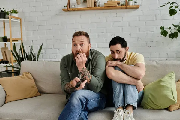 Due uomini barbuti con le braccia incrociate siedono strettamente su un divano in un soggiorno, trasudando un senso di comfort e compagnia.. — Foto stock