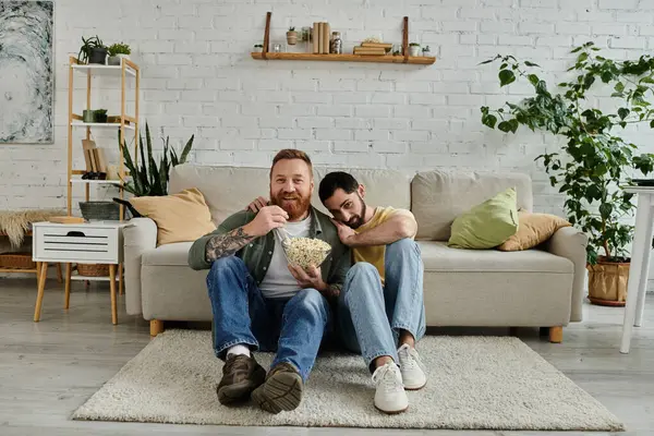 A couple of bearded men sitting comfortably on top of a couch in their living room. — Stock Photo