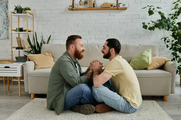 Due uomini con la barba seduti sul pavimento di fronte a un divano, godendo di tempo di qualità insieme in un accogliente soggiorno. — Foto stock