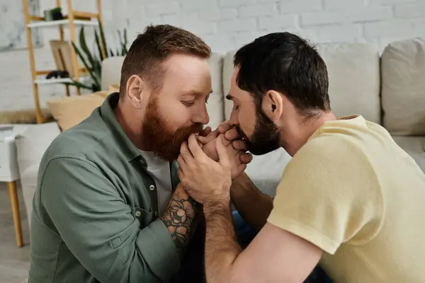 Two men, both bearded, are comfortably seated side by side on top of a couch in a living room. — Stock Photo