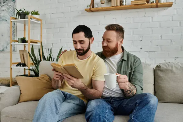 Two bearded men sitting on a couch, engrossed in a book, spending quality time together in their living room. — Stock Photo