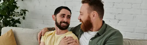 Un paio di uomini con la barba si siedono comodamente su un divano, godendo del tempo di qualità insieme in un soggiorno. — Foto stock