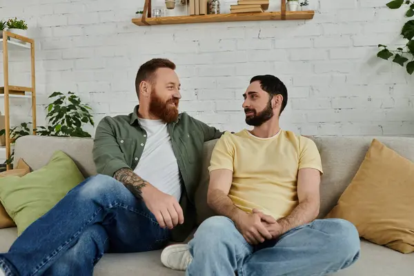 Couple gay barbu assis sur un canapé, engagé dans une conversation sincère dans un cadre confortable salon. — Photo de stock