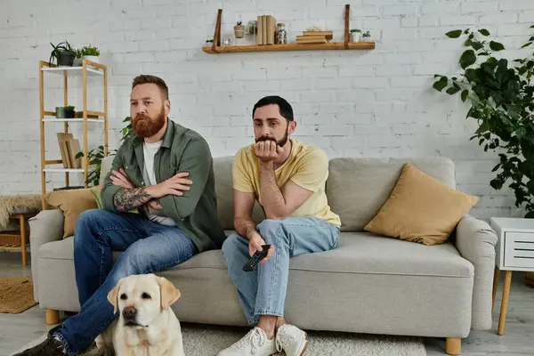Due uomini con la barba seduti su un divano, godendo di tempo di qualità con il loro Labrador in un accogliente soggiorno. — Foto stock
