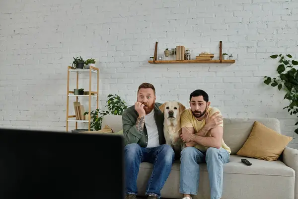Two men, a gay couple, sit on a couch in a living room, enjoying the company of their labrador retriever. — Stock Photo