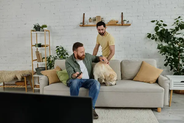 Un hombre con barba sentado en un sofá, abrazando cariñosamente a un perro labrador en una cálida y acogedora sala de estar. - foto de stock