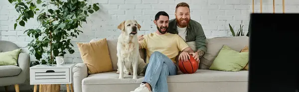 Two men with beards enjoy quality time on couch with friendly labrador in cozy living room. — Stock Photo