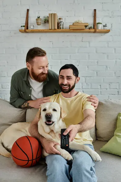 Bearded gay couple enjoying a cozy moment on a couch with their labrador in a living room. — Stock Photo